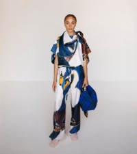 Mannequin portant un haut foulard et un pantalon en soie à imprimé cygne multicolore, ainsi que le sac Peg en maille à carreaux.