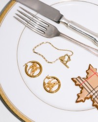 Shot of Dining plate, with 2 pieces of Cutlery, the Burberry EKD Hoop Earrings in Gold and the Shield Bracelet​ in Gold