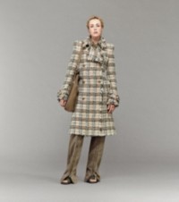 Modelo usando um casaco xadrez Burberry Check com calças com detalhes de zíper e uma bolsa tote Shield Twin pequena