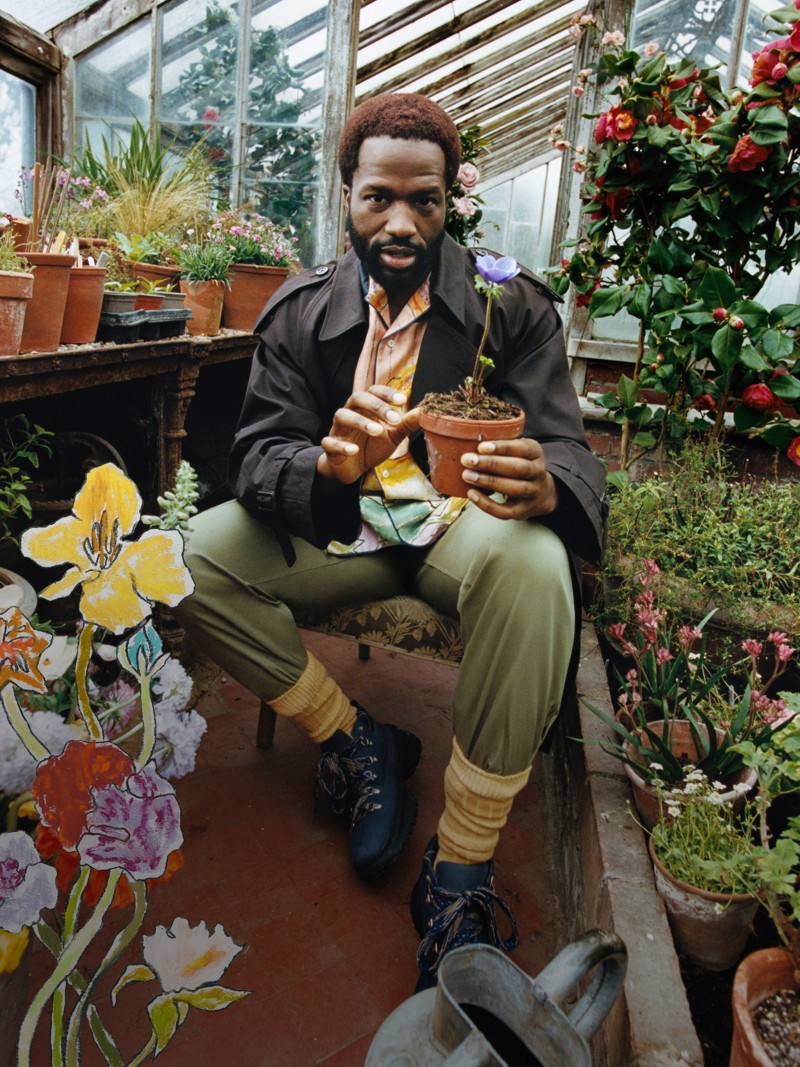 British actor Sope Dirisu wearing Burberry Trench Coat holding a plant pot in a green house