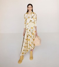 Una modelo luce un conjunto de camisa y falda color sherbet con estampado de dientes de león, combinado con el bolso Peg en tejido a cuadros y las botas Marsh color crema.