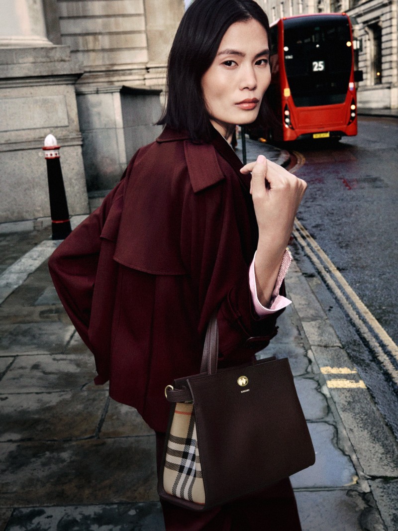 Shot of model wearing the Cropped Wool Mayfair Trench Jacket in colour Vineyard red holding the Small Cotswolds Check Tote in colour Vineyard red