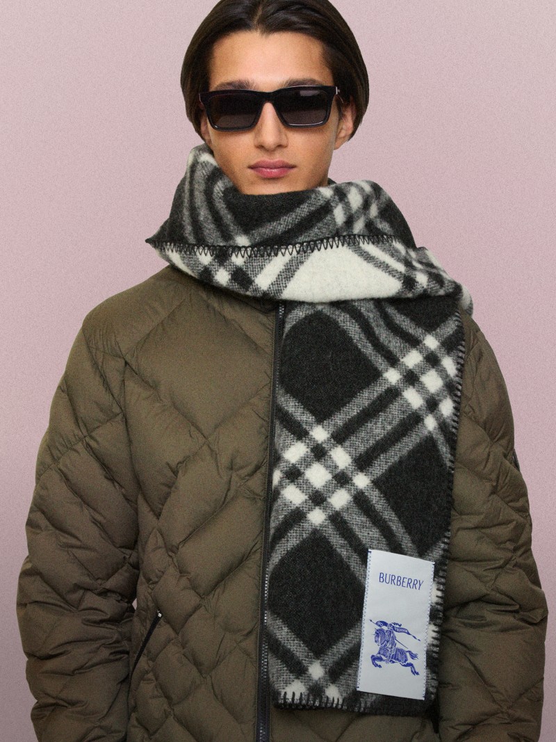 Person mit Sonnenbrille, schwarzweißem Schal in Check und olivfarbener Steppjacke.