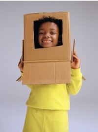 Boy wearing yellow top and trouser, holding a cardboard box over his head, where his head is showing through a cut out hole