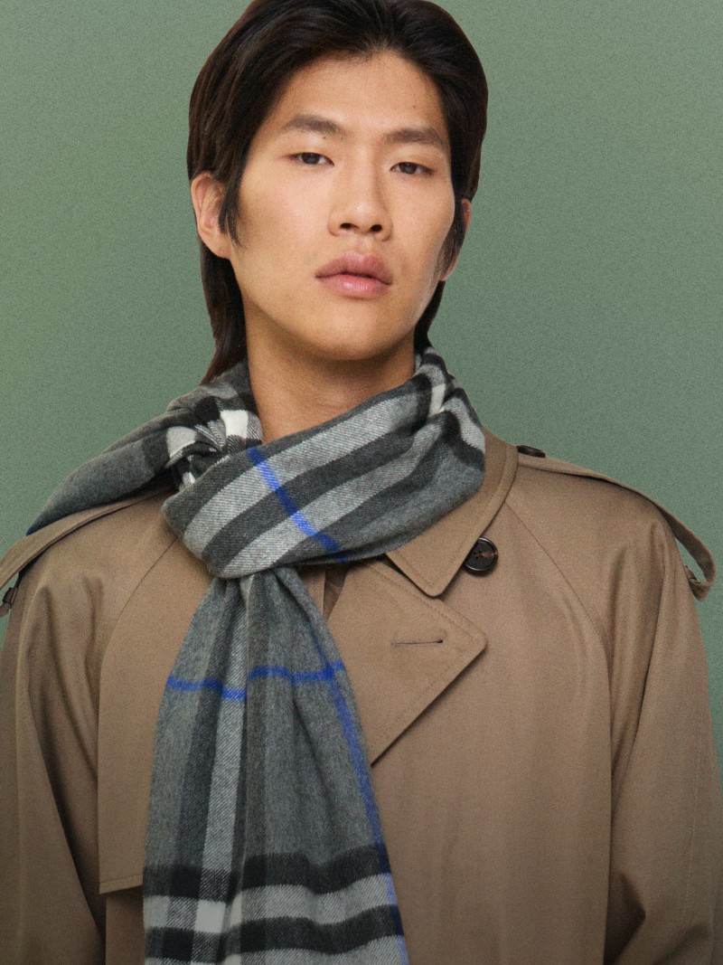 Person wearing a grey check-pattern cashmere scarf with blue accents and a beige trench coat.