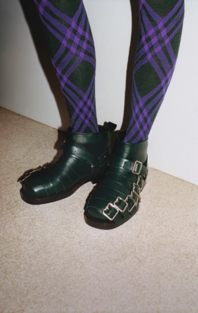 Campanha Inverno 2023 da Burberry apresentando modelo usando botas com tiras de couro em Vine e meia-calça de lã stretch xadrez em Royal e Vine 